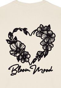 Maglione crema con un disegno ricamato nero di un cuore intrecciato con fiori e il testo "Bloom Mood" sottostante.
