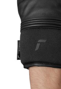Guanto in pelle nera con polsino in tessuto nero testurizzato, caratterizzato da un accento logo liscio. Il design include cuciture visibili e una vestibilità aderente.