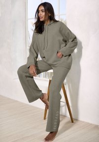 Übergroßer graugrüner Hoodie und passende weite Hosen, aus weichem Stoff gefertigt, mit einer Vorderasche und dezentem Logo-Detail am Bein.