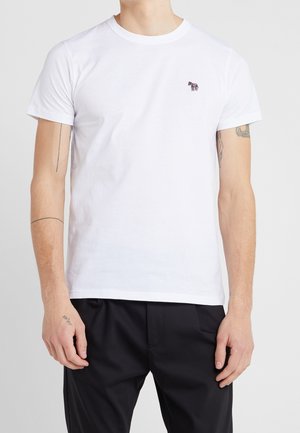 Biała bawełniana koszulka z dekoltem okrągłym, krótkimi rękawami i małym, wielokolorowym haftem zebry na lewej piersi. Zestawiona z czarnymi spodniami.