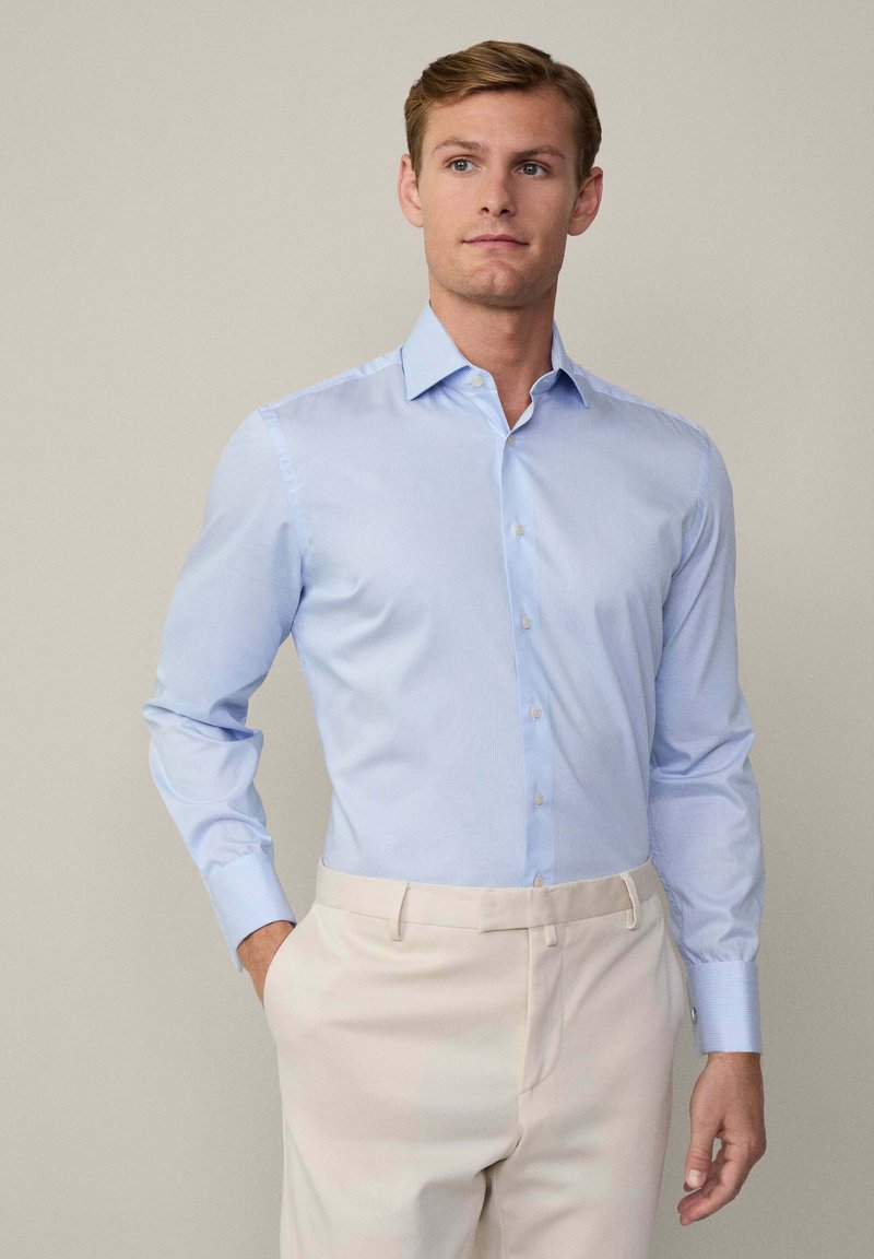 Lichtblauwe, gestreepte overhemd met lange mouwen en een button-down kraag. Gemaakt van een gladde stof, gecombineerd met beige broeken.