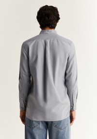 Camicia da uomo button-up di colore grigio chiaro, con maniche lunghe, colletto standard e polsini abbottonati, caratterizzata da una texture di tessuto liscia.