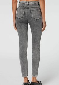 Dopasowane szare dżinsy o wyblakłej fakturze, posiadające tylne kieszenie i średni stan. Nogawki są lekko skrócone.