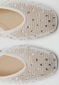 Scarpe in rete di pizzo color beige chiaro con decorazioni di gemme trasparenti. Punta arrotondata e bordo elasticizzato per una vestibilità sicura. Superficie testurizzata.