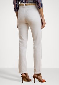 White straight-leg jeans made of denim, featuring back pockets, a high waistband, and worn with brown and orange heeled sandals.