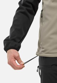 Veste avec une manche noire et un corps gris clair ; elle comprend un cordon de serrage à la taille, une poche zippée et des poignets élastiques.