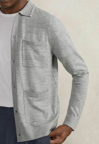 Grauer Strickcardigan mit einem Kragen-Design, vorderem Knopfverschluss und zwei aufgesetzten Taschen. Glatte Textur mit einem Look aus gemischtem Garn.