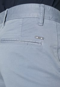 Light blue trousers made of smooth fabric feature a stitched waistband, back pocket with a horizontal design, and a small metal logo accent.