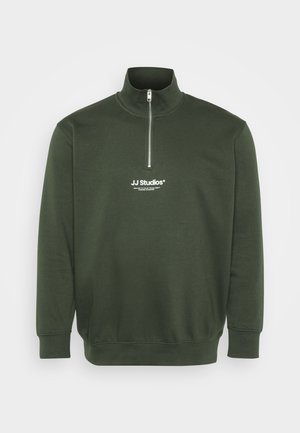 Ciemnozielona bluza z wysokim kołnierzem i krótkim zamkiem, z białym logo JJ Studios na piersi. Wykonana z miękkiej, teksturowanej tkaniny.