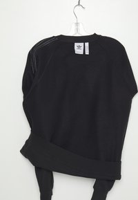 Crna dukserica s dugim rukavima, rebrastim manžetama i širokim krojem. Ima bijele šavove i Adidasov logotip označen na zadnjem dijelu ovratnika.