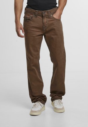 Brown denim jeans with a relaxed fit, featuring contrast stitching, five pockets, and a button-and-zip closure. Worn with light-colored sneakers.