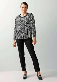 Zwart-wit gestreept shirt met lange mouwen en een ronde halslijn, gecombineerd met zwarte slim-fit broeken en zwarte schoenen met een kettingaccent.