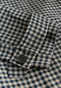 Chemise en coton à carreaux bleu marine et crème avec détails de poignets à boutons. Présente un motif à carreaux classique et une texture lisse.