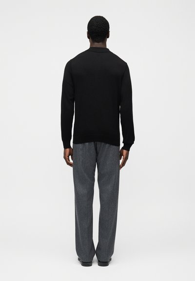 Μαύρο πουκάμισο με μακρύ μανίκι και ριμπ μανσέτες, σε συνδυασμό με γκρι παντελόνι φαρδιάς γραμμής με κάθετες ρίγες. Το ύφασμα φαίνεται υφασμάτινο και απαλό.