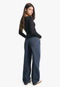 Černý top s dlouhým rukávem doplněný modrými džíny s vysokým pasem a širokými nohavicemi. Džíny mají dvě zadní kapsy a robustní pas.