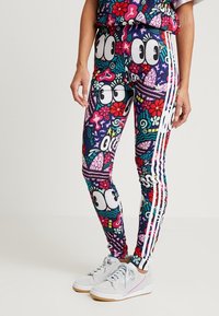 Leggings med färgglada tecknade ögon, blommor och abstrakta former, med vita Adidas-stripes på sidorna, bära med vita sneakers.