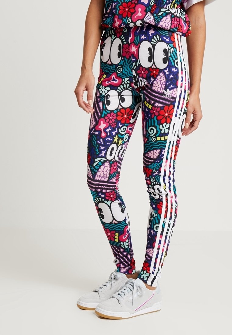 Leggings med färgglada tecknade ögon, blommor och abstrakta former, med vita Adidas-stripes på sidorna, bära med vita sneakers.