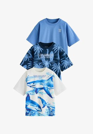 Trois t-shirts à manches courtes : un bleu clair, un marine avec des palmiers, et un blanc avec des requins bleus et un texte sur les requins blancs.