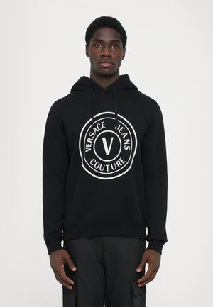 Mustallaneest valmistatud kapuuts, millel on suur valge ümmargune logo, millel on tekst "VERSACE JEANS COUTURE" ja keskel "V". Kapuutsi kinnitusnöör, soonikuga mansetid.