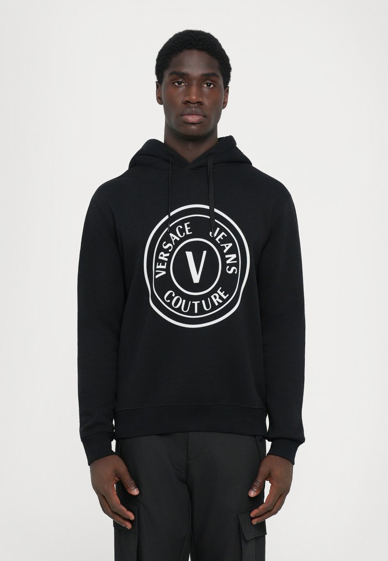 Mustallaneest valmistatud kapuuts, millel on suur valge ümmargune logo, millel on tekst "VERSACE JEANS COUTURE" ja keskel "V". Kapuutsi kinnitusnöör, soonikuga mansetid.