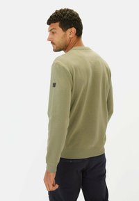 Oliwkowa bluza z ribbowymi mankietami i dołem, uproszczony design, z małym czarnym logo na lewym rękawie. Pokazana z tyłu.