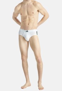 Slip bianchi con una texture liscia, dotati di un ampio elastico in vita e tre strisce nere. Progettati per una vestibilità aderente e comfort.