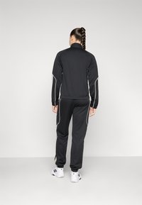 Fato de treino atlético preto com riscas laterais brancas, apresentando um casaco de gola alta e calças ajustadas. Projetado para conforto e movimento.