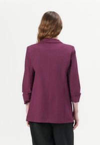 Violetti, räätälöity bleiseri, jossa on kaulus, kolmanneksen mittaiset hihat ja suora leikkaus. Sujuva pinta, jossa on takasauman yksityiskohtia.