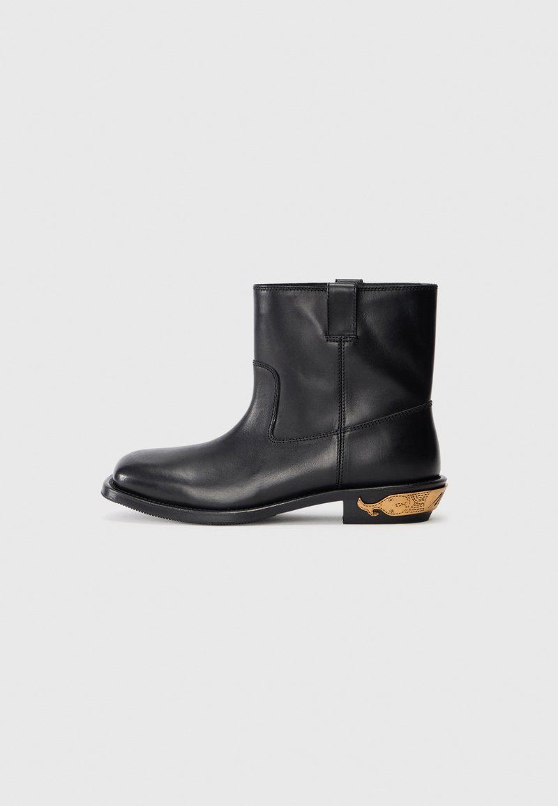 Svart läderankelboot med en slät yta, rund tå och en guldaccentuerad valmotiv på hälen. Minimalistisk design.