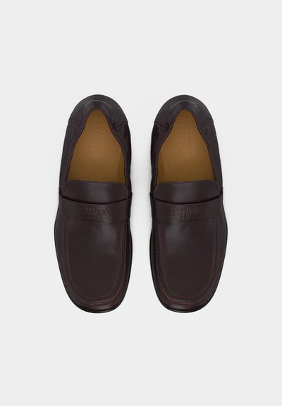 Ζευγάρι σκουρόκαφέ δερμάτινων loafers χωρίς κορδόνια, με στρογγυλεμένες τετράγωνες μύτες και ραμμένα διακοσμητικά στοιχεία, εμφανιζόμενα από πάνω σε λευκό φόντο.
