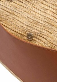 Vævet stråtaske med tan læderdetaljer, cirkulær form og metal snap-lukning. Har en tekstureret overflade og kontrasterende materialer.