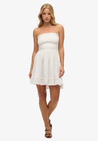 Biała sukienka bez ramiączek z marszczonym stanem, rozkloszowaną spódnicą i warstwowym dołem. Wykonana z lekkiego materiału, charakteryzuje się subtelną teksturą i falbanami.
