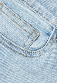 Un tissu en denim bleu clair avec une poche au bord supérieur arrondi. Coutures visibles de couleur beige contrastante autour de la poche et des coutures.
