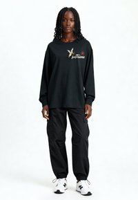 T-shirt noir à manches longues avec texte « je t'aime » et graphique de cupidon, associé à un pantalon cargo noir fuselé et des baskets blanches.