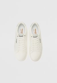 Vita sneakers med en slät läderliknande yta, rund tå, platta snören och en svart "Wrangler"-logotyp på sidan. Innersula i minnesskum.