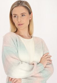 Pastelizēta gradienta kardigāns, kas piedāvā rozā, zilo un baltu krāsu sajaukumu, ar mīkstu adītu tekstūru, atvērtu priekšpusi un ribotām piedurknēm.
