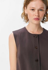Robe brune élégante sans manches avec un col arrondi et trois boutons marron sur le devant. Texture de tissu lisse.