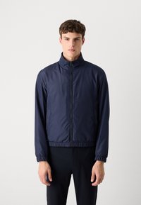 Navy blue bomber jacket with a stand-up collar, elastic cuffs, and waistband; made of smooth, lightweight material. Minimalist design.