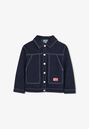 Veste en jean indigo foncé avec coutures blanches, col pointu, poches avant, et un patch logo rouge sur la poche inférieure. Boutons argentés.