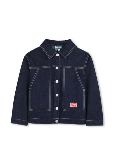 Veste en jean indigo foncé avec coutures blanches, col pointu, poches avant, et un patch logo rouge sur la poche inférieure. Boutons argentés.