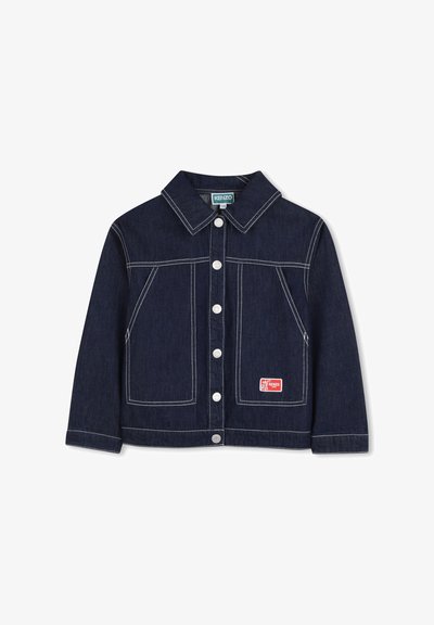 Veste en jean indigo foncé avec coutures blanches, col pointu, poches avant, et un patch logo rouge sur la poche inférieure. Boutons argentés.