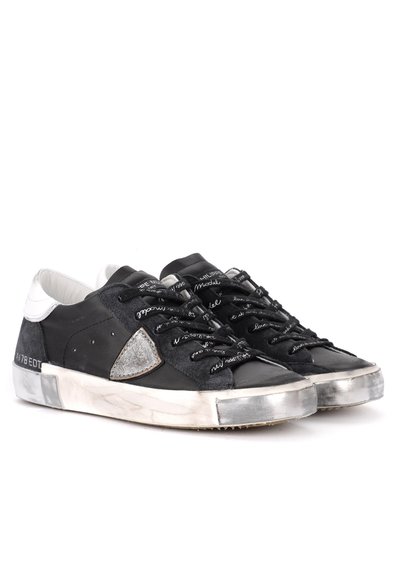 Baskets noires en mélange de cuir et de daim, avec un accent triangulaire argenté, des lacets noirs et une semelle blanche usée.