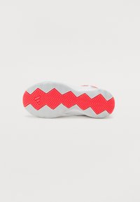 Semelle de chaussure avec une base blanche et un motif de bande de roulement en zigzag prononcé ; présente des accents roses néon dans un design en chevrons.