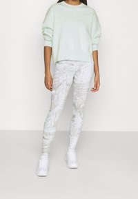 Ljus mintgrön sweatshirt i lös passform; mönstrade vita leggings med iriserande detaljer; vita sneakers fulländar outfiten.