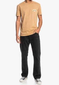 Tan bavlněné tričko s potiskem vpředu, spárované s černými kordovými kalhotami a černobílými teniskami. Jednoduchý, neformální design.