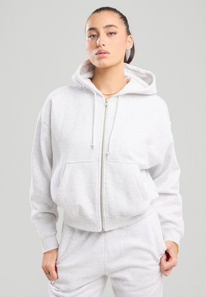 Grau Zip-Hoodie aus weichem Material, mit einer Fronttasche, Kordeln und lässiger Passform. Kombiniert mit passenden grauen Jogginghosen.