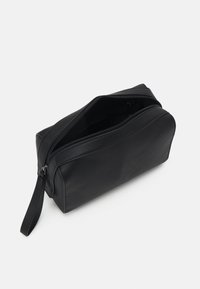 Trousse de toilette rectangulaire noire avec fermeture à glissière sur le dessus, en matériau synthétique lisse, dotée d'une poignée latérale pour un transport facile.