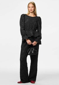 Zwarte, gestructureerde stof outfit met een peplum top, lange mouwen en bijpassende broek. Bevat een kleine zwarte tas en rode schoenen.