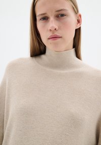 Beige ribbel turtleneck trui met een zachte textuur en een ontspannen pasvorm, met een hoge hals en lange mouwen.