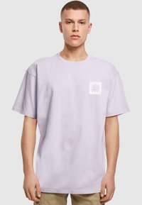 Lys lavendel bomulds t-shirt med korte ærmer, afslappet pasform og en firkantet hvid lomme med et blomstergrafik på venstre bryst.